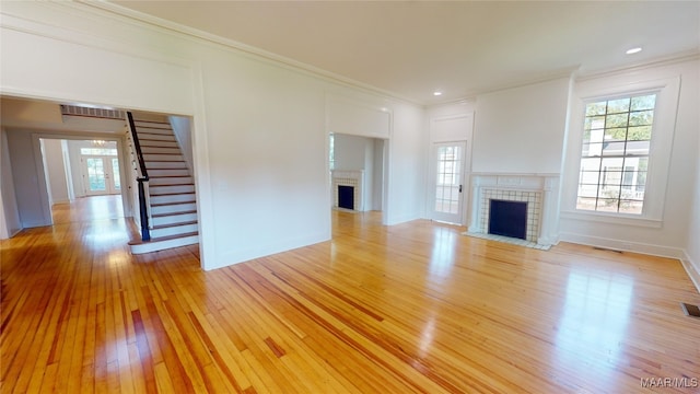 unfurnished living room featuring a brick fireplace, stairs, light wood-style flooring, and a healthy amount of sunlight
