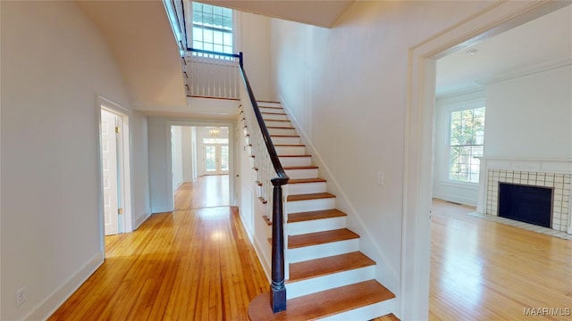 stairway featuring baseboards, wood finished floors, a high ceiling, and a fireplace