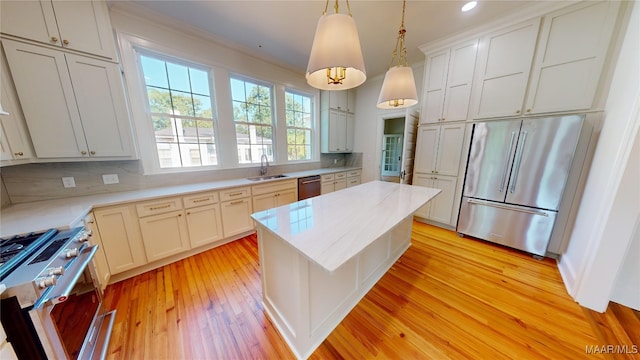 kitchen featuring stainless steel appliances, a kitchen island, a sink, light wood-type flooring, and pendant lighting
