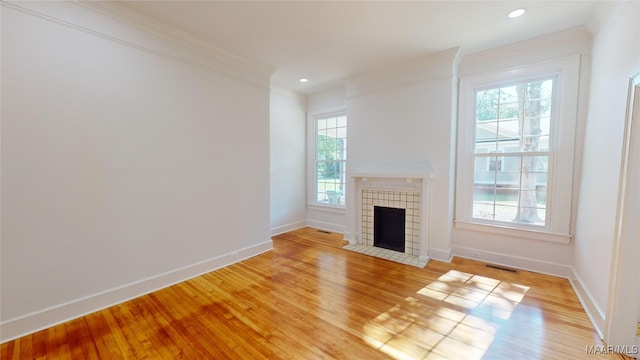 unfurnished living room featuring a tile fireplace, light wood-style floors, ornamental molding, baseboards, and visible vents