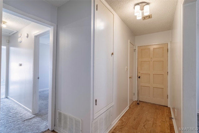 corridor featuring light wood-type flooring and a textured ceiling