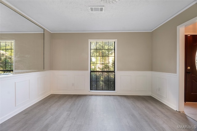 empty room featuring light wood-type flooring, a wealth of natural light, a textured ceiling, and ornamental molding