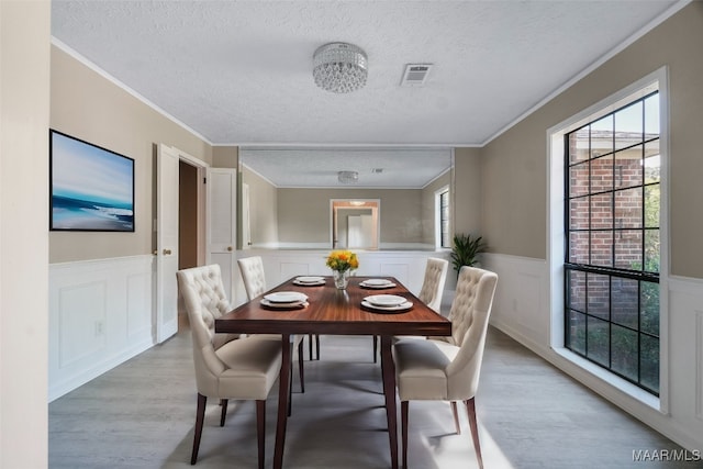 dining space with light wood-type flooring, a textured ceiling, a healthy amount of sunlight, and ornamental molding