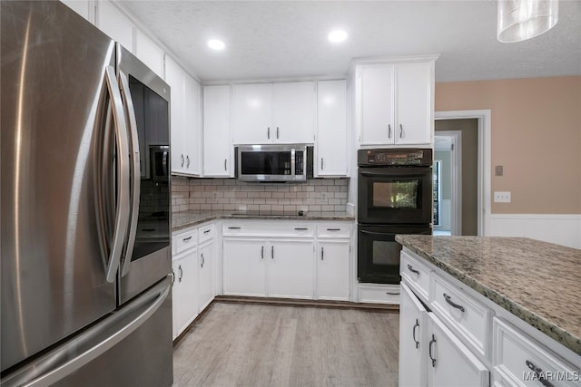 kitchen with light wood-type flooring, a textured ceiling, black appliances, light stone counters, and white cabinets