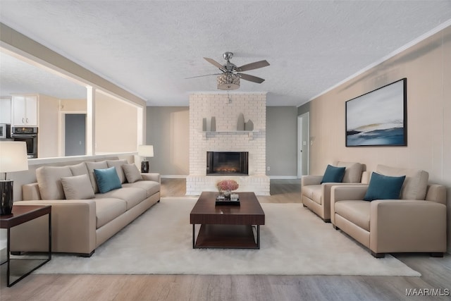 living room featuring a textured ceiling, ceiling fan, light wood-type flooring, and a fireplace