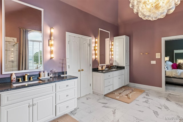 ensuite bathroom with marble finish floor, two vanities, connected bathroom, a sink, and baseboards