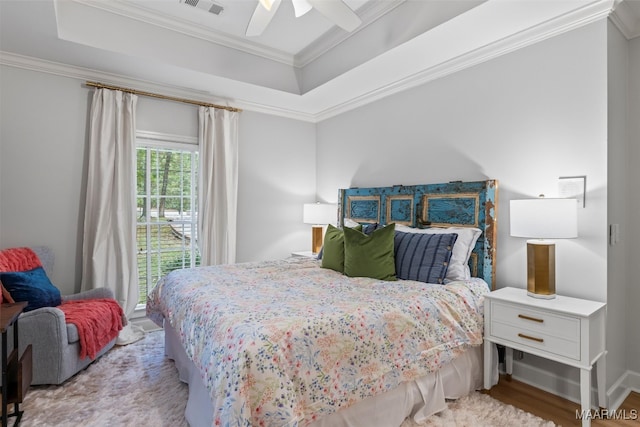 bedroom with a ceiling fan, a raised ceiling, crown molding, and light wood finished floors