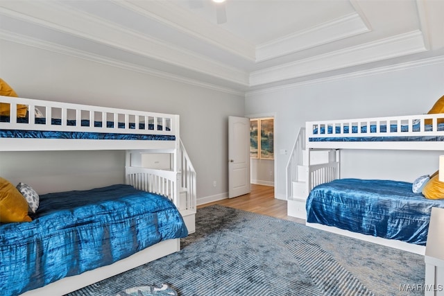 bedroom with baseboards, ceiling fan, wood finished floors, a tray ceiling, and crown molding