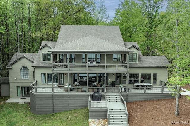 rear view of property with brick siding, a shingled roof, stairway, and a balcony