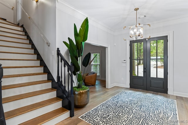 foyer with light wood finished floors, stairs, crown molding, french doors, and a chandelier