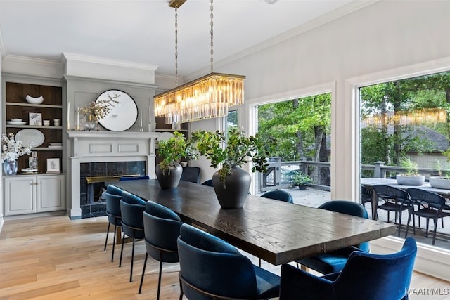 dining room featuring ornamental molding, a tile fireplace, a chandelier, and light wood-style flooring