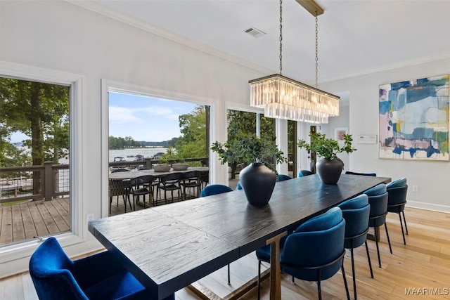 dining space featuring light wood-style flooring, crown molding, a water view, visible vents, and an inviting chandelier