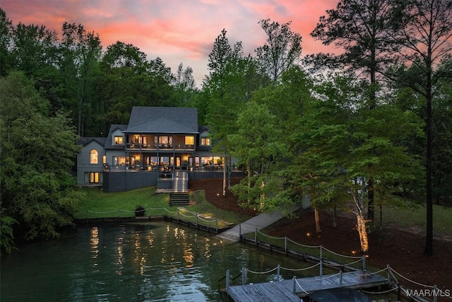 back of property at dusk featuring a water view, a balcony, stairway, and a lawn