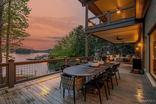 wooden terrace with outdoor dining area, a water view, ceiling fan, and an outdoor living space