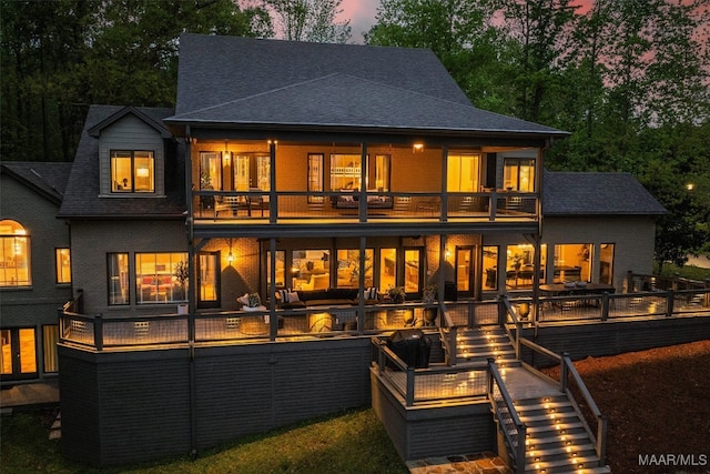 back of house at dusk featuring a balcony, stairway, a deck, and brick siding