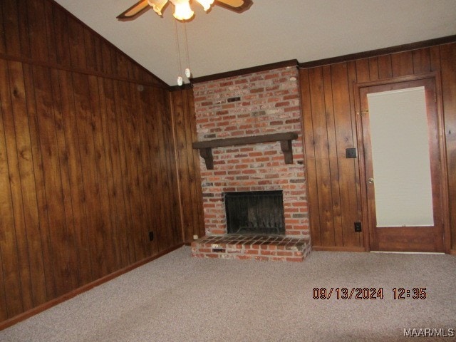 unfurnished living room with a brick fireplace, wood walls, ceiling fan, and carpet flooring