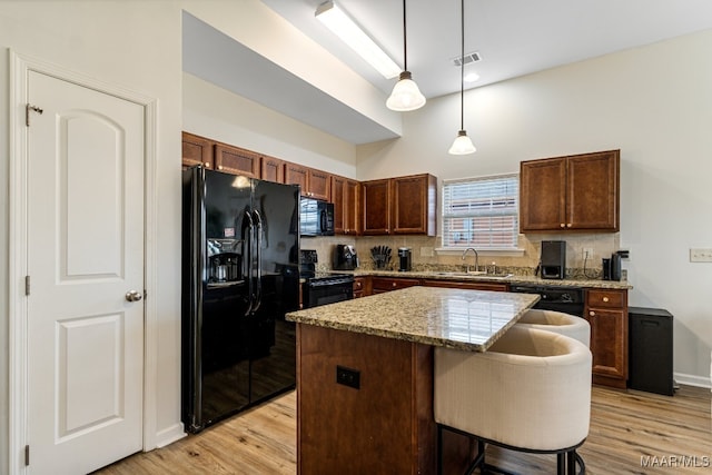 kitchen with light hardwood / wood-style flooring, black appliances, a center island, decorative backsplash, and hanging light fixtures