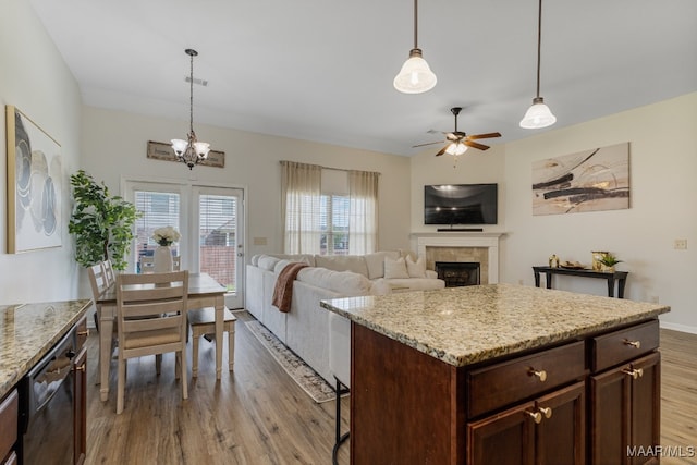 kitchen with a center island, ceiling fan with notable chandelier, a tiled fireplace, and light hardwood / wood-style floors