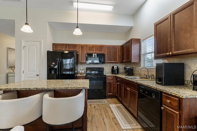 kitchen featuring light hardwood / wood-style flooring, a kitchen bar, black appliances, sink, and decorative backsplash