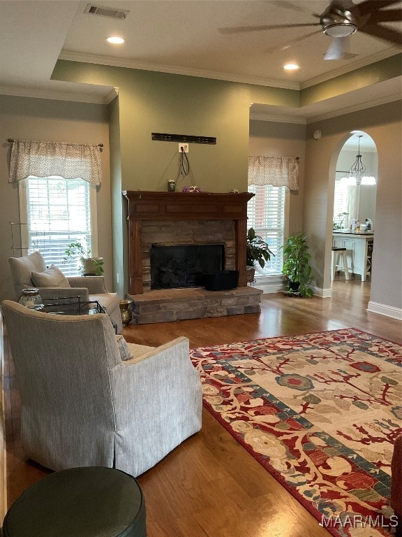 living room featuring wood-type flooring, a fireplace, crown molding, and ceiling fan