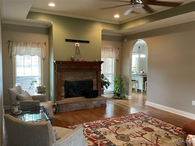 living room featuring ceiling fan, a stone fireplace, ornamental molding, and hardwood / wood-style floors