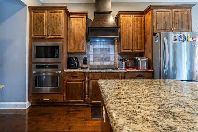 kitchen featuring appliances with stainless steel finishes, tasteful backsplash, light stone counters, custom range hood, and dark wood-type flooring