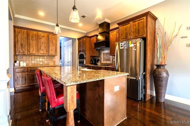 kitchen featuring backsplash, stainless steel fridge, a kitchen island with sink, and custom exhaust hood