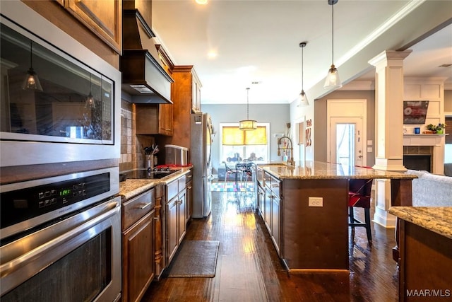 kitchen with a center island with sink, a kitchen breakfast bar, light stone countertops, appliances with stainless steel finishes, and decorative columns