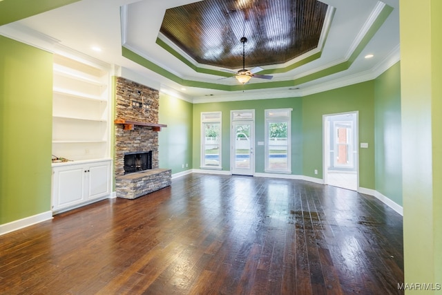 unfurnished living room featuring dark hardwood / wood-style flooring, a raised ceiling, a stone fireplace, built in features, and ceiling fan