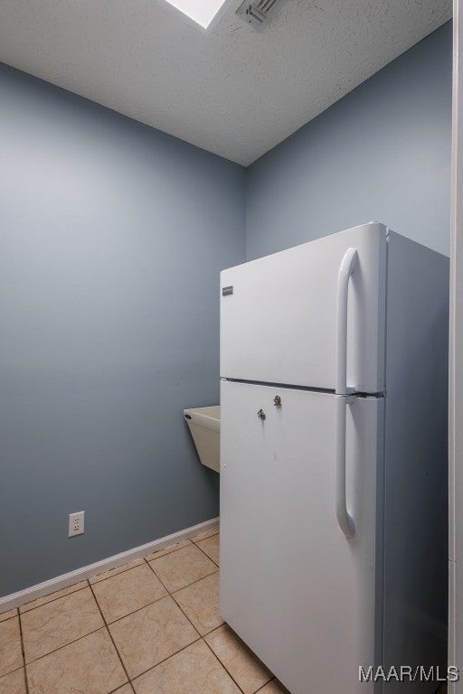 interior space with a textured ceiling, light tile patterned flooring, and white fridge