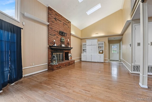 unfurnished living room featuring light wood finished floors, baseboards, a fireplace, a skylight, and high vaulted ceiling