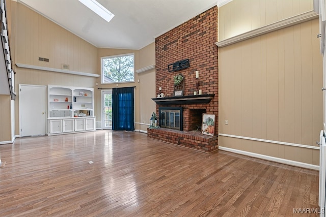 unfurnished living room featuring wood walls, wood-type flooring, a skylight, a fireplace, and high vaulted ceiling