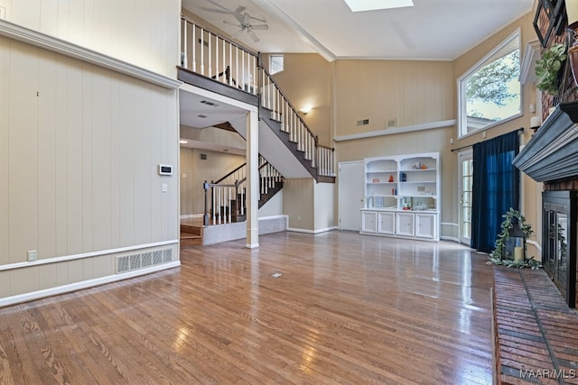 unfurnished living room featuring wood walls, wood-type flooring, a brick fireplace, ceiling fan, and a high ceiling