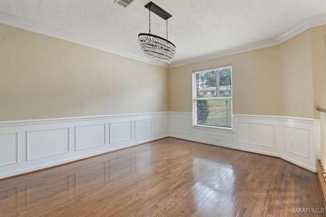 unfurnished room with a wainscoted wall, a textured ceiling, wood finished floors, crown molding, and a chandelier