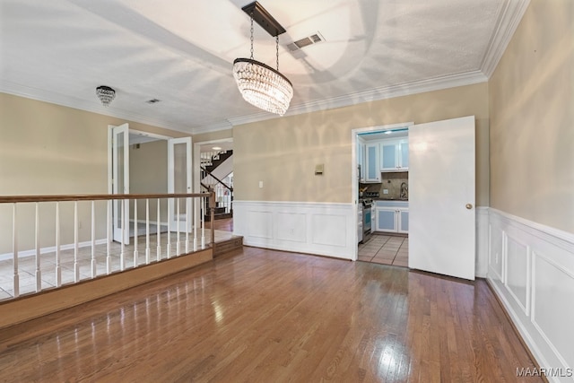 spare room featuring crown molding, hardwood / wood-style flooring, and an inviting chandelier