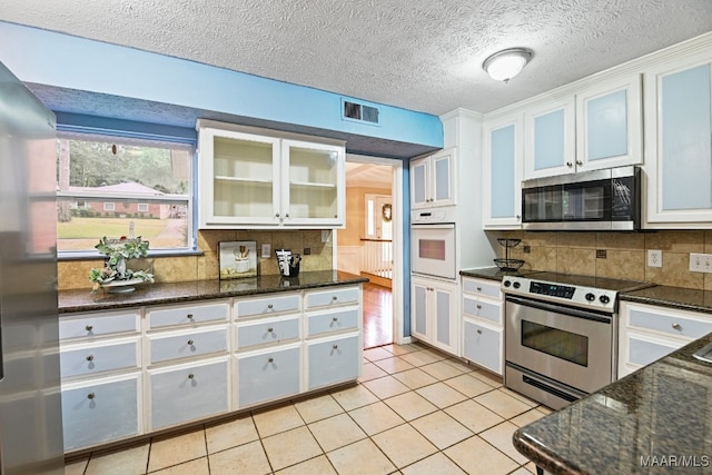 kitchen featuring tasteful backsplash, white cabinetry, stainless steel appliances, dark stone countertops, and light tile patterned floors