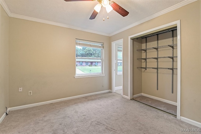 unfurnished bedroom with a closet, crown molding, light colored carpet, a textured ceiling, and ceiling fan