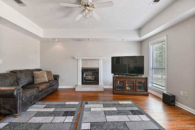 living room featuring ceiling fan, a fireplace, dark hardwood / wood-style flooring, and a textured ceiling