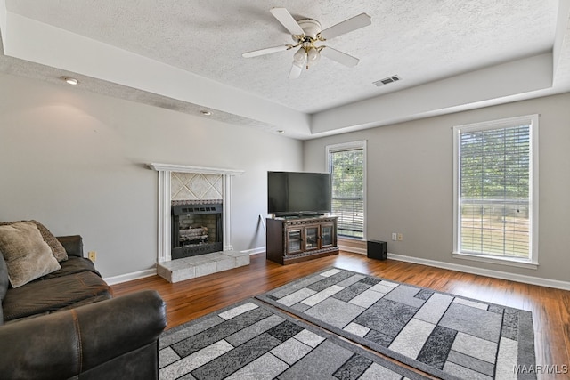 living room with a textured ceiling, wood-type flooring, ceiling fan, and a tile fireplace