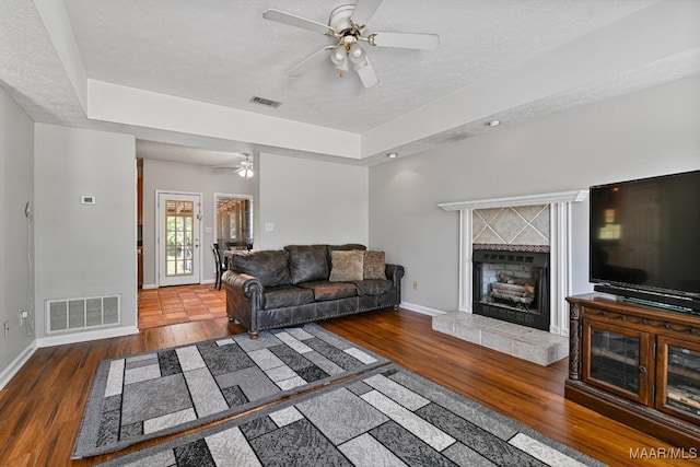 living room with a fireplace, a raised ceiling, dark wood-type flooring, ceiling fan, and a textured ceiling