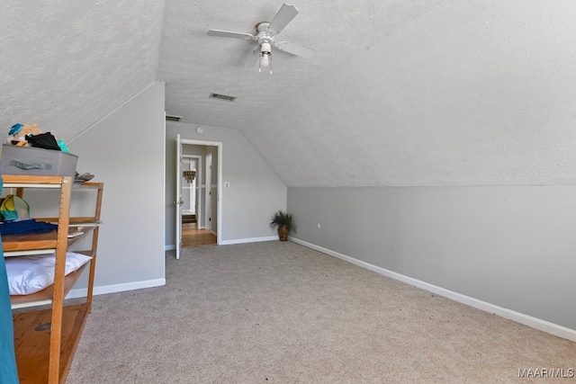 additional living space with lofted ceiling, ceiling fan, light carpet, and a textured ceiling