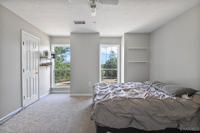 bedroom with multiple windows, ceiling fan, light colored carpet, and a textured ceiling