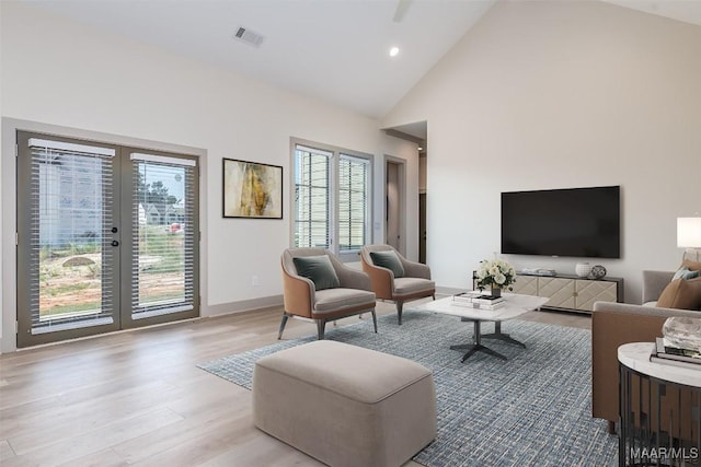 living room with french doors, high vaulted ceiling, and light wood-type flooring