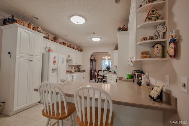 kitchen with white cabinets, white refrigerator with ice dispenser, kitchen peninsula, a kitchen bar, and a textured ceiling