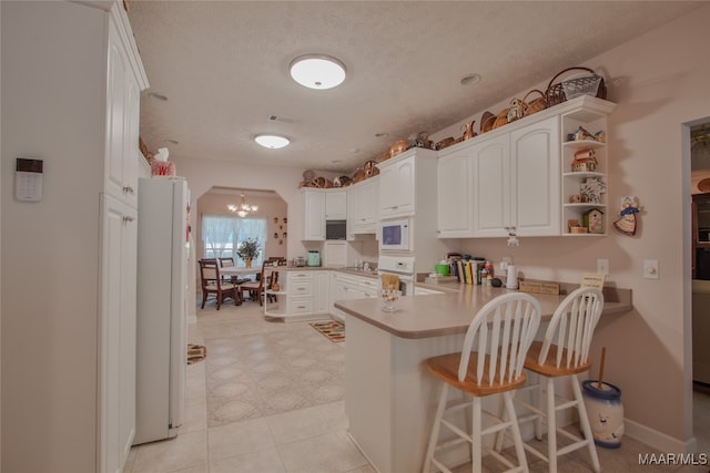 kitchen with white appliances, kitchen peninsula, white cabinets, and a textured ceiling