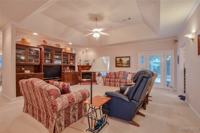 living room with crown molding, a raised ceiling, ceiling fan, and light colored carpet