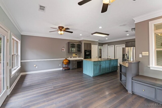 kitchen with dark wood-type flooring, an island with sink, ornamental molding, ceiling fan, and stainless steel fridge