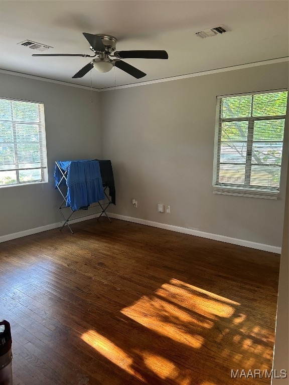 empty room with ornamental molding, ceiling fan, plenty of natural light, and dark wood-type flooring