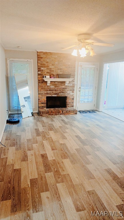 unfurnished living room with ceiling fan, a fireplace, a textured ceiling, and light hardwood / wood-style flooring