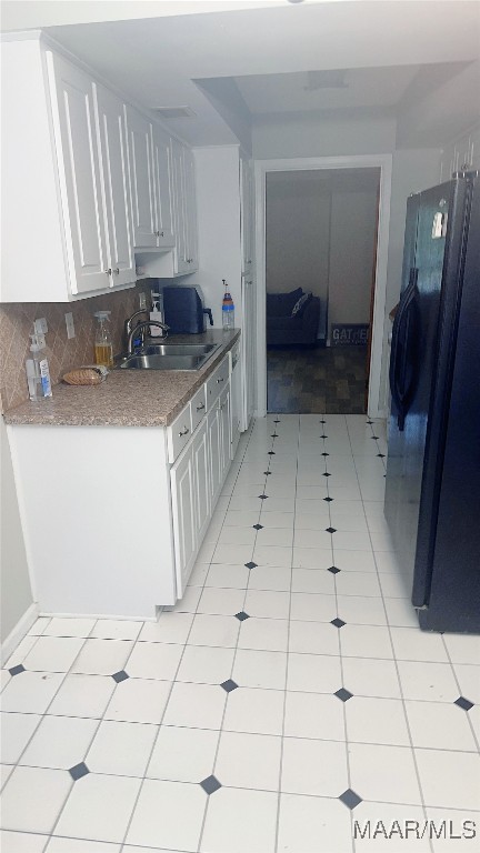 kitchen featuring light tile patterned floors, white cabinetry, black refrigerator, and sink